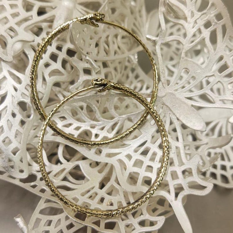 May include: A pair of gold hoop earrings with a textured snake design. The earrings are on a white background.
