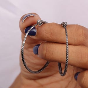 May include: A pair of silver hoop earrings with snake head accents. The earrings are textured and have a slightly oxidized finish.