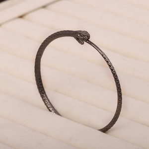 Puede incluir: Un brazalete negro en forma de serpiente con un acabado texturizado.