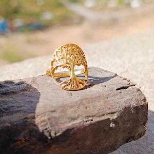 Puede incluir: Un anillo dorado con un diseño de árbol de la vida. El anillo tiene forma ovalada y un diseño delicado e intrincado.