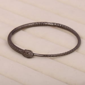 May include: A black snake-shaped bangle bracelet with a textured finish.