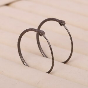 May include: A pair of black snake hoop earrings. The earrings are made of metal and have a textured finish. The snake heads are facing forward.