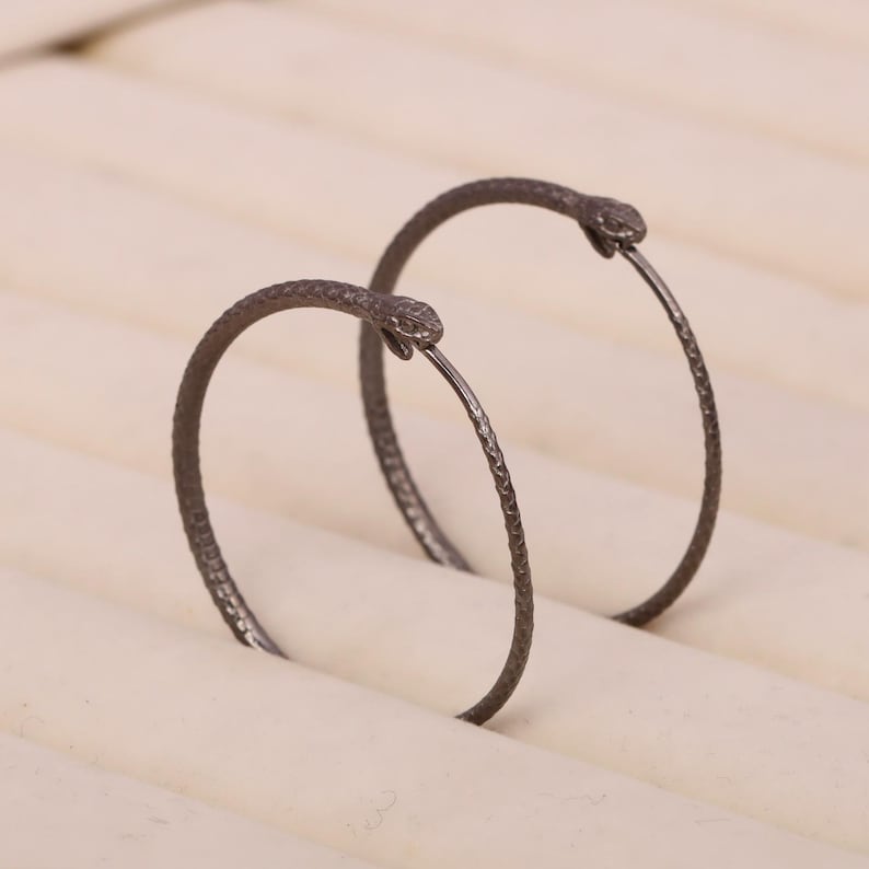 May include: A pair of black snake hoop earrings. The earrings are made of metal and have a textured finish. The snake heads are facing forward.