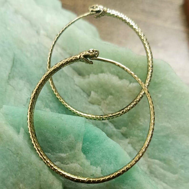 May include: A pair of gold hoop earrings with a snake head design. The earrings are textured and have a shiny finish.