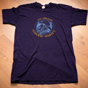 May include: A navy blue t-shirt with a circular graphic that says "The Original Seafood Shanty" in yellow text.