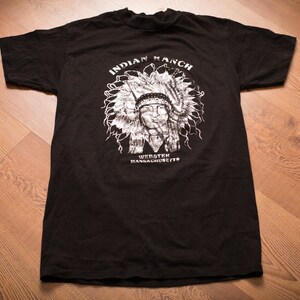May include: Black t-shirt with a white graphic of a Native American wearing a headdress. The text "INDIAN RANCH" and "WORCESTER MASSACHUSETTS" are printed below the graphic.