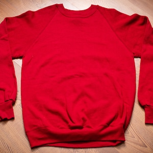 May include: A red sweatshirt with a crew neck and long sleeves. The sweatshirt has a raglan style with a contrasting color on the sleeves.