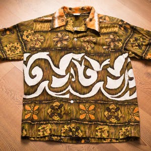May include: A short-sleeved button-up shirt with a brown, white, and orange patterned design. The shirt has a white collar and a button-up front.