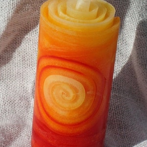 Könnte beinhalten: Eine rote und orangefarbene Spiralkerze mit einem weißen Docht. Die Kerze ist aus Wachs und hat ein Spiralmuster.