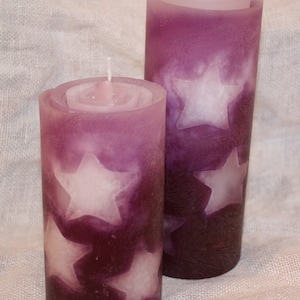 Könnte beinhalten: Zwei violette Kerzen mit weißen Sternenmustern. Die Kerzen stehen auf einer weißen Leinenoberfläche.