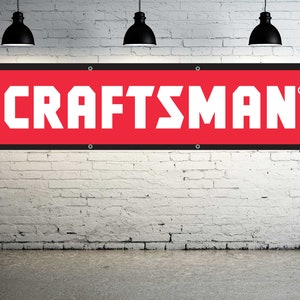 May include: A red banner with white text that reads "CRAFTSMAN" with a registered trademark symbol. The banner is hanging on a white brick wall.