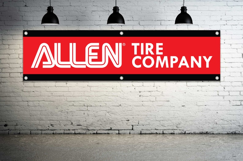 May include: A rectangular banner with the text "ALLEN TIRE COMPANY" in white lettering. The banner has a red background with a black border and is mounted on a white brick wall. Three black pendant lights hang above.