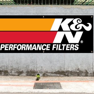 May include: Black and white K&N Performance Filters banner with a red and orange stripe design. The banner is hanging on a gray concrete wall.