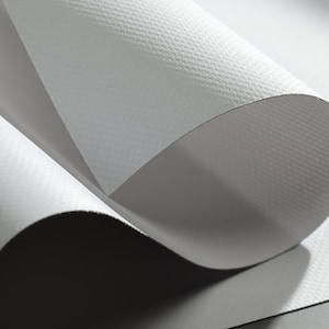 May include: Close-up of a rolled-up, textured, white paper. The paper has a subtle, grid-like pattern and is partially unrolled, revealing a smooth, gray interior. The lighting creates shadows and highlights, emphasizing the paper's texture.