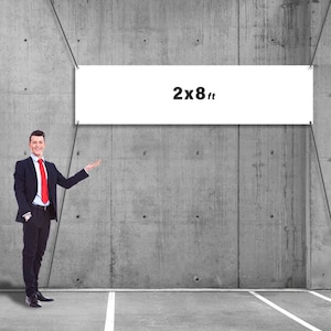 May include: A white banner with the text "2x8 ft" is suspended against a gray concrete wall. A man in a black suit and red tie stands to the left, gesturing towards the banner. The banner is 2 feet high and 8 feet wide.