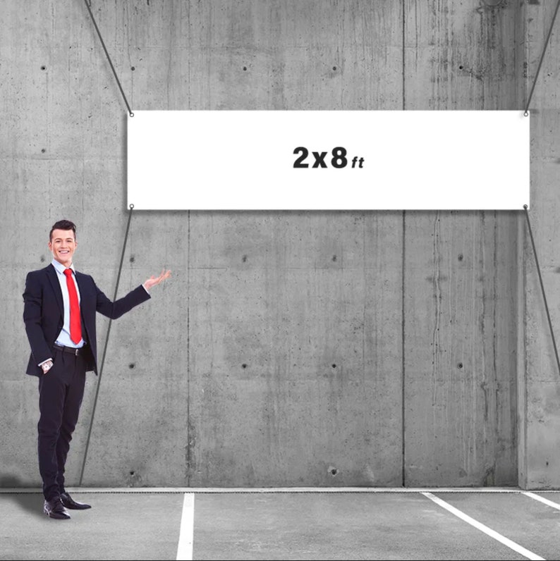 May include: A white banner with the text "2x8 ft" is suspended against a gray concrete wall. A man in a black suit and red tie stands to the left, gesturing towards the banner. The banner is 2 feet high and 8 feet wide.