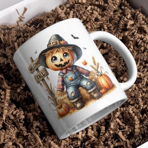 May include: White ceramic mug with a colorful illustration of a scarecrow with a pumpkin head. The scarecrow is sitting on a bale of hay and holding a pumpkin. The mug has the words "Welcome Fall" on a sign.