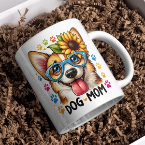 May include: White ceramic mug with a colorful illustration of a corgi wearing blue glasses and a sunflower on its head. The text "DOG MOM" is printed on the mug.