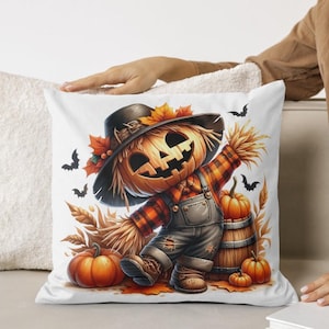 May include: A white pillow with a colorful illustration of a scarecrow with a pumpkin head. The scarecrow is wearing overalls and a plaid shirt. There are pumpkins and fall leaves around the scarecrow.