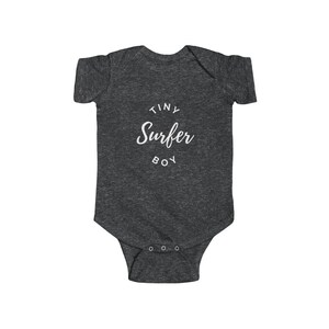 Puede incluir: Un body de beb&eacute; gris oscuro con texto blanco que dice "Tiny Surfer Boy" en un c&iacute;rculo.