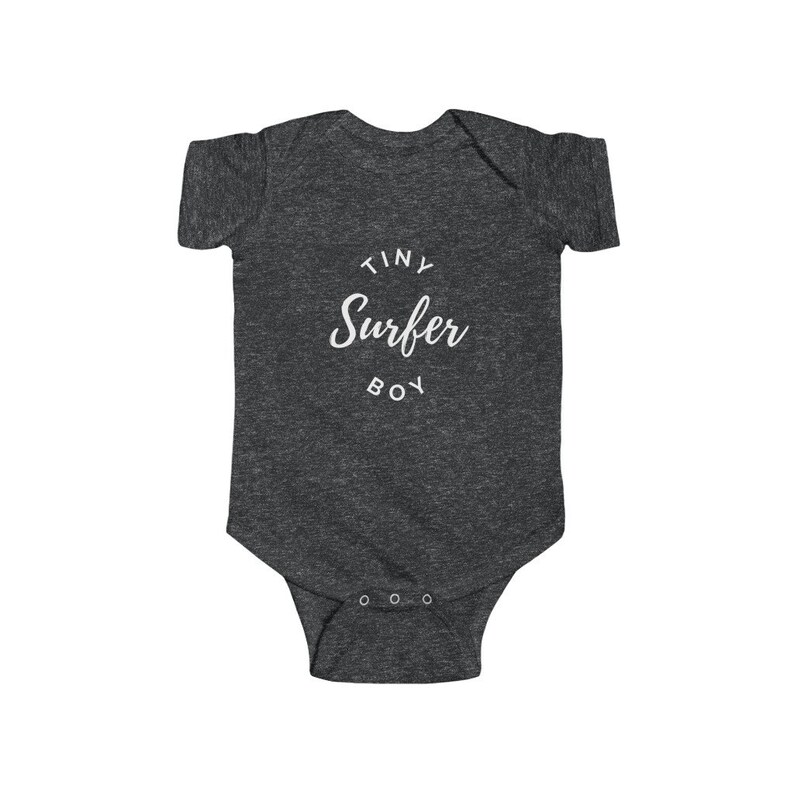 Puede incluir: Un body de beb&eacute; gris oscuro con texto blanco que dice "Tiny Surfer Boy" en un c&iacute;rculo.