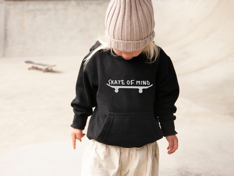 May include: A black hooded sweatshirt with a white graphic of a skateboard and the text "Skate of Mind". The model is wearing a beige beanie.
