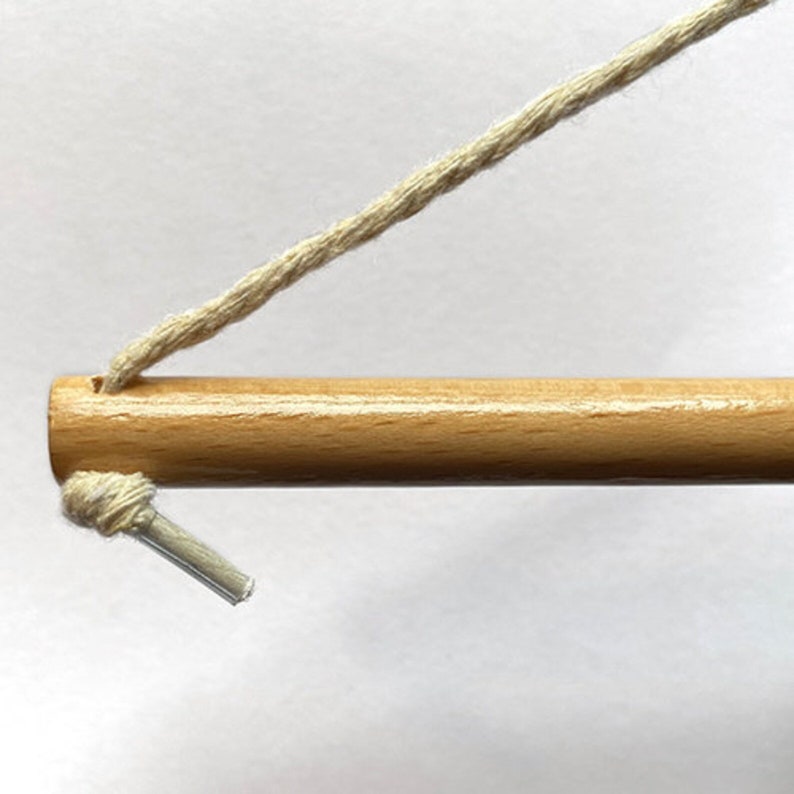 May include: A close-up of a wooden dowel rod with a white string attached to one end. The string is tied in a knot and has a small plastic loop at the end.