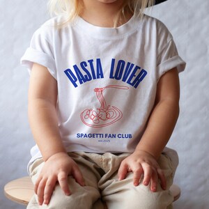 May include: A white t-shirt with blue and red text that says "PASTA LOVER" and "SPAGHETTI FAN CLUB est. 2025". A red and white illustration of spaghetti is in the center of the shirt.