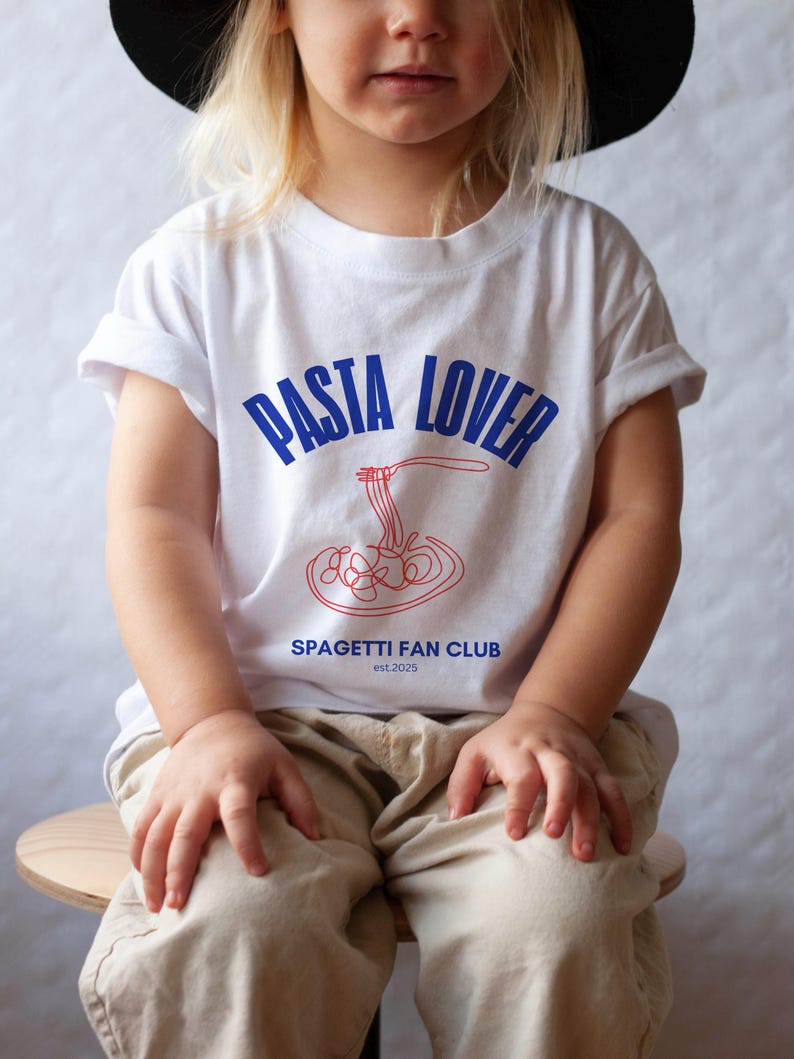May include: A white t-shirt with blue and red text that says "PASTA LOVER" and "SPAGHETTI FAN CLUB est. 2025". A red and white illustration of spaghetti is in the center of the shirt.