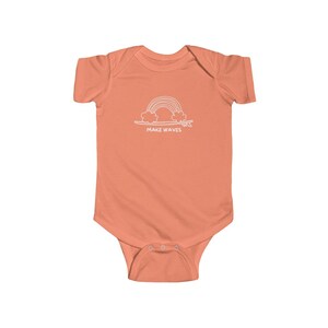 May include: A coral orange baby onesie with a white outline of a rainbow over a surfboard and the text "MAKE WAVES".