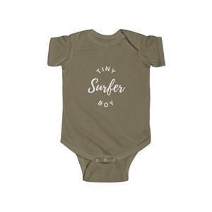 Puede incluir: Un body de beb&eacute; color caqui con el texto "Tiny Surfer Boy" en blanco.