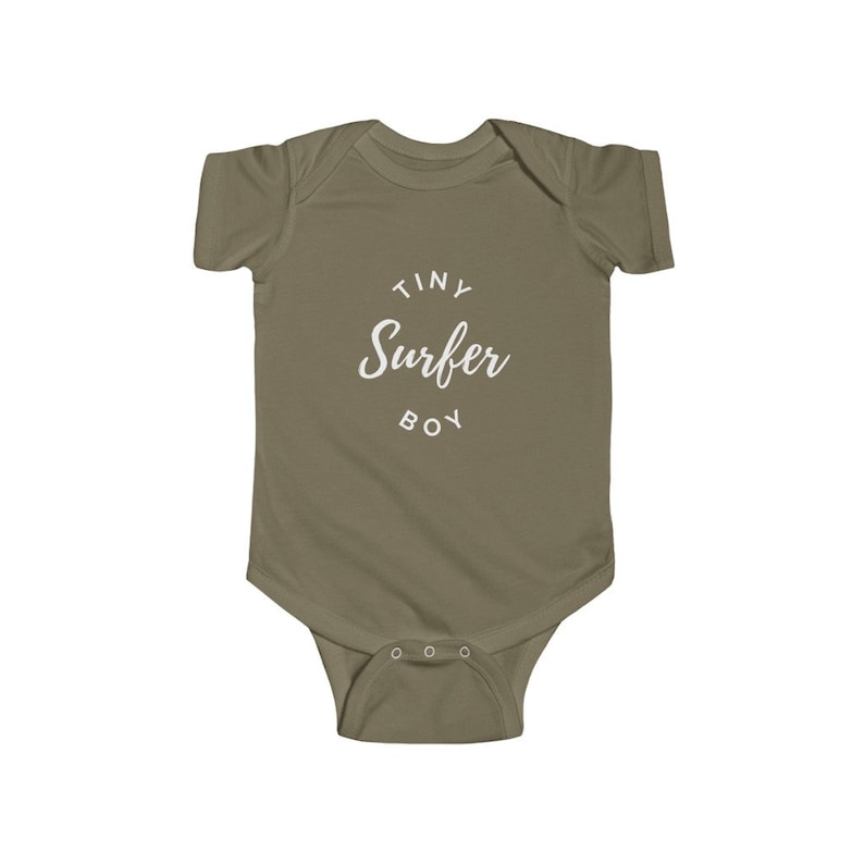 Puede incluir: Un body de beb&eacute; color caqui con el texto "Tiny Surfer Boy" en blanco.