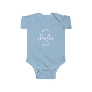 Puede incluir: Uniforme de beb&eacute; azul claro con texto blanco que dice "Tiny Surfer Boy".