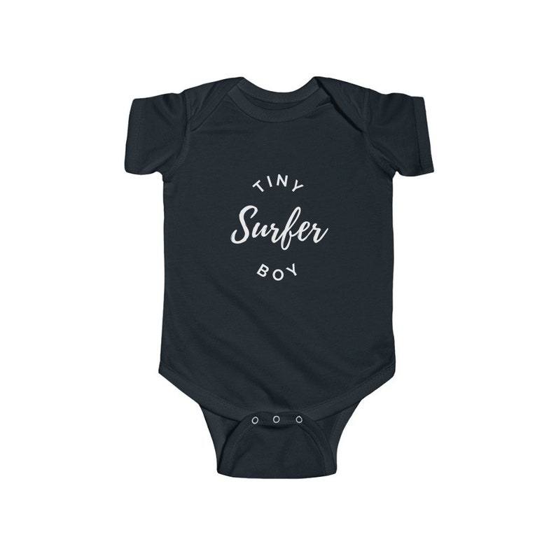 Puede incluir: Un body de beb&eacute; azul oscuro con texto blanco que dice "Tiny Surfer Boy" en un c&iacute;rculo.