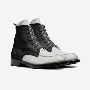 May include: A pair of black and white leather boots. The boots feature a textured, snake-like pattern on the white sections and smooth black leather on the upper. They have black laces and a small black heel.