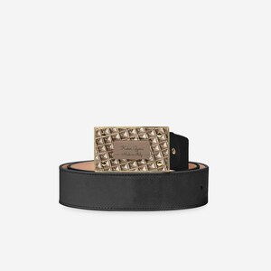 Può includere: Una cintura in pelle nera con fibbia rettangolare color oro. La fibbia presenta un motivo geometrico con piccole borchie dorate e un'etichetta marrone con testo. La cintura è larga circa 3,8 cm.