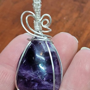 May include: A teardrop-shaped amethyst gemstone wrapped in silver wire, with a decorative silver wire bail.