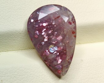 May include: A teardrop-shaped gemstone with a faceted cut. The gemstone is translucent and has a pink and purple hue with iridescent glitter throughout.