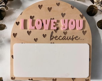 Può includere: Segno in legno con un messaggio rosa "Ti amo perché..." Il segno ha un ritaglio a forma di cuore e uno spazio vuoto per scrivere.
