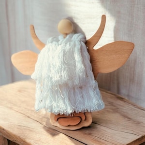 May include: A wooden cow's head wall hanging with a white fringe trim. The cow head is made of light brown wood and has a simple, minimalist design.