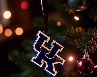 Può includere: Un ornamento blu e oro per l'albero di Natale con il logo "UK" ad incastro, appeso a un nastro scuro. L'ornamento è su un albero di Natale con altre decorazioni e luci.