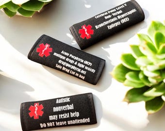 Può includere: Tre braccialetti di allerta medica neri con testo bianco e un simbolo medico rosso. I braccialetti elencano condizioni mediche tra cui paralisi cerebrale, porfiria acuta e autismo. Il testo include avvertenze e istruzioni.