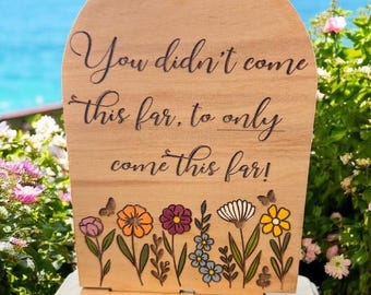 Può includere: Cartello in legno con la citazione "You didn't come this far, to only come this far!" e una farfalla. Il cartello presenta un design floreale con fiori colorati. Il cartello è realizzato in legno chiaro.
