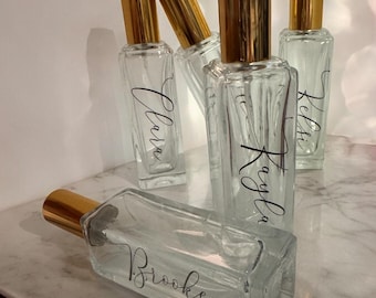 Può includere: Cinque bottiglie di vetro trasparente con spruzzini dorati ed etichette personalizzate. Le etichette riportano i nomi Kayla, Kelsi, Clara, Brooke e un altro nome parzialmente oscurato.