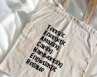 Può includere: Una borsa di tela beige con testo nero che dice "Terrific, Energetic, Amazing, Caring, Hardworking, Enthusiastic, Reliable".