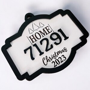 Puede incluir: Adorno navideño negro y blanco con el texto "HOME" y el número "71291" sobre un fondo blanco. El adorno también incluye el texto "Christmas 2023".