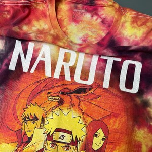 May include: A tie-dye t-shirt in shades of red, orange, and yellow featuring the word NARUTO in large white letters. Below the text is a graphic illustration of three anime characters and a large fox creature with multiple tails in the background.