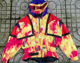 May include: A vibrant yellow and hot pink tie-dye patterned jacket with a purple hood and black accents. The jacket features a front zipper closure, long sleeves with elastic cuffs, a drawstring waist, and the word Salomon printed on the front.