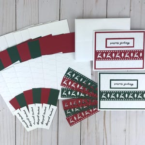 A Christmas card kit with white embossed cardstock with a Christmas tree pattern, red and green cardstock mats, red and green die cut reindeer borders, and 6 stamped "Seasons Greetings" sentiments in black in. A set of white cards and envelopes completes the kit.