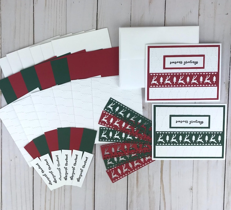 A Christmas card kit with white embossed cardstock with a Christmas tree pattern, red and green cardstock mats, red and green die cut reindeer borders, and 6 stamped "Seasons Greetings" sentiments in black in. A set of white cards and envelopes completes the kit.